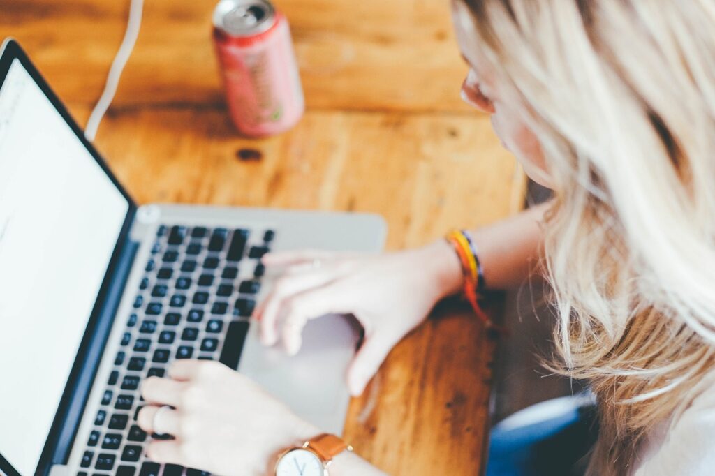 Woman with blond hair using silver laptop for work, on a wooden desk.